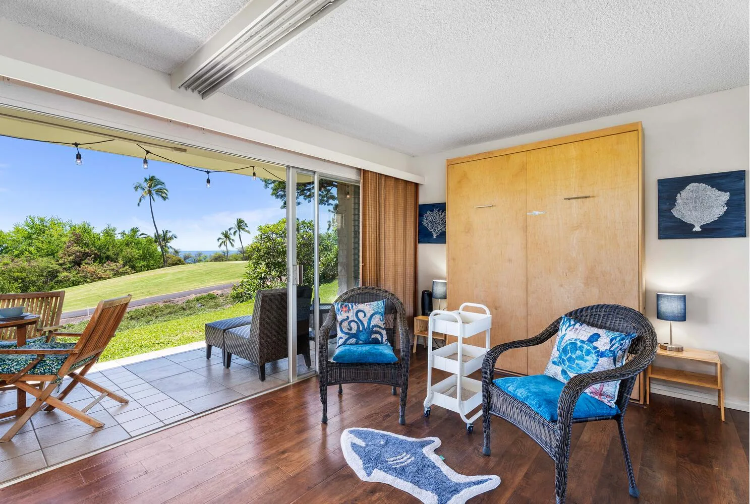Una habitación luminosa se abre a un patio, con asientos de mimbre y vistas al exterior.