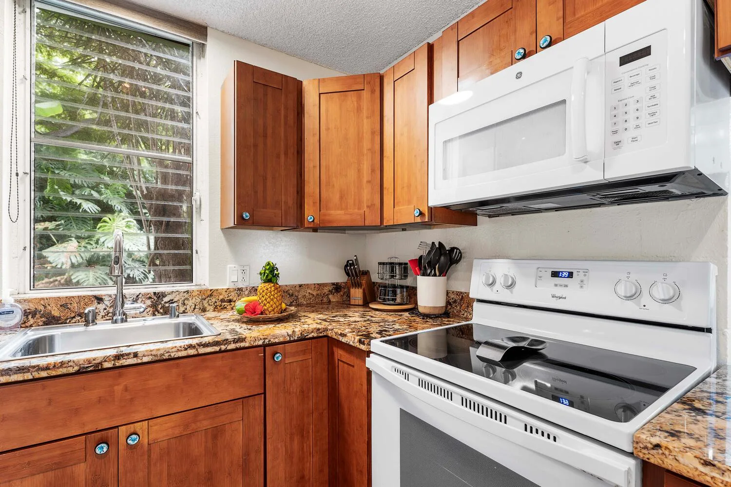 Una cocina con gabinetes de madera, un fregadero y una estufa bajo un microondas.