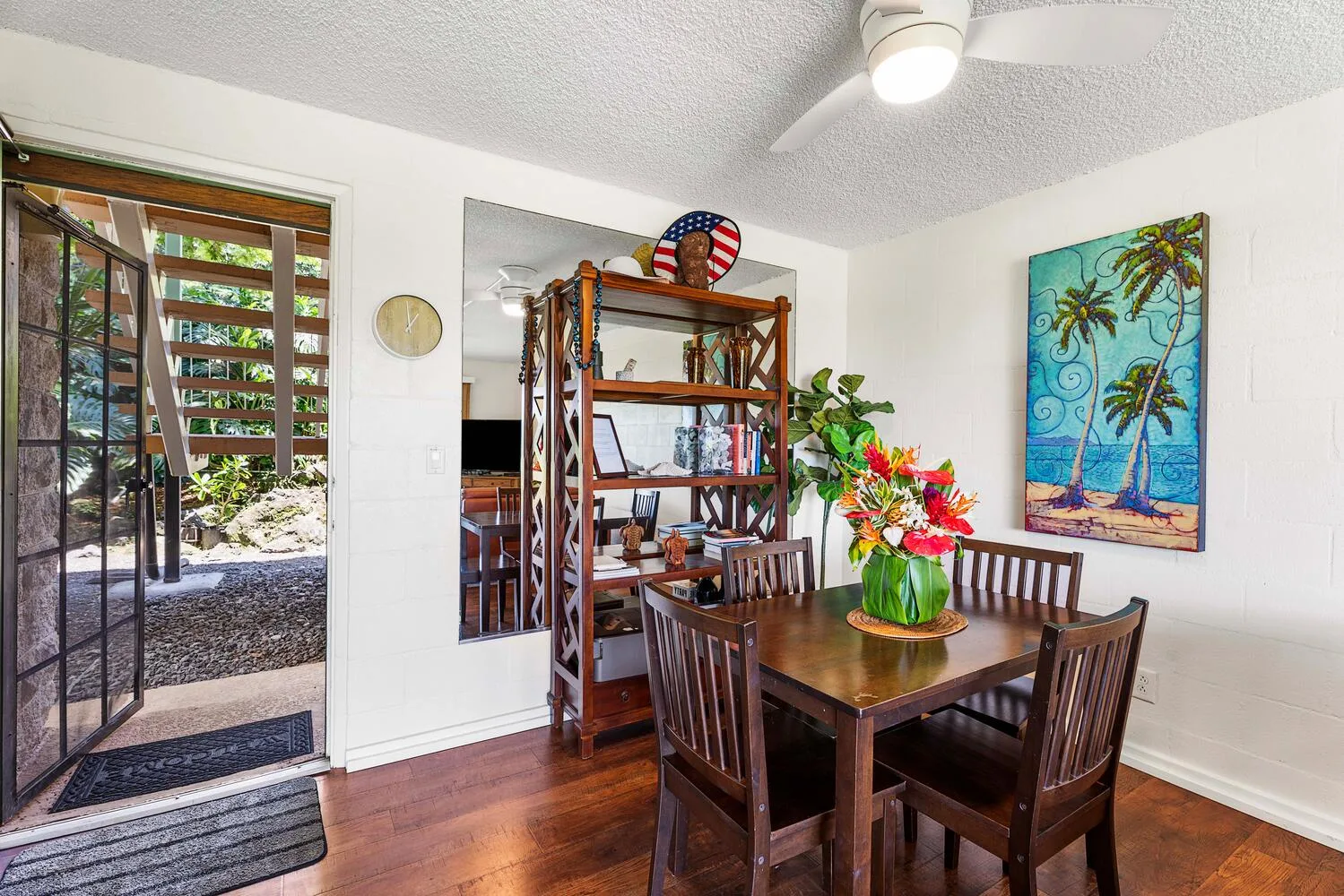 Un comedor con una mesa de madera, sillas y arte tropical colorido.