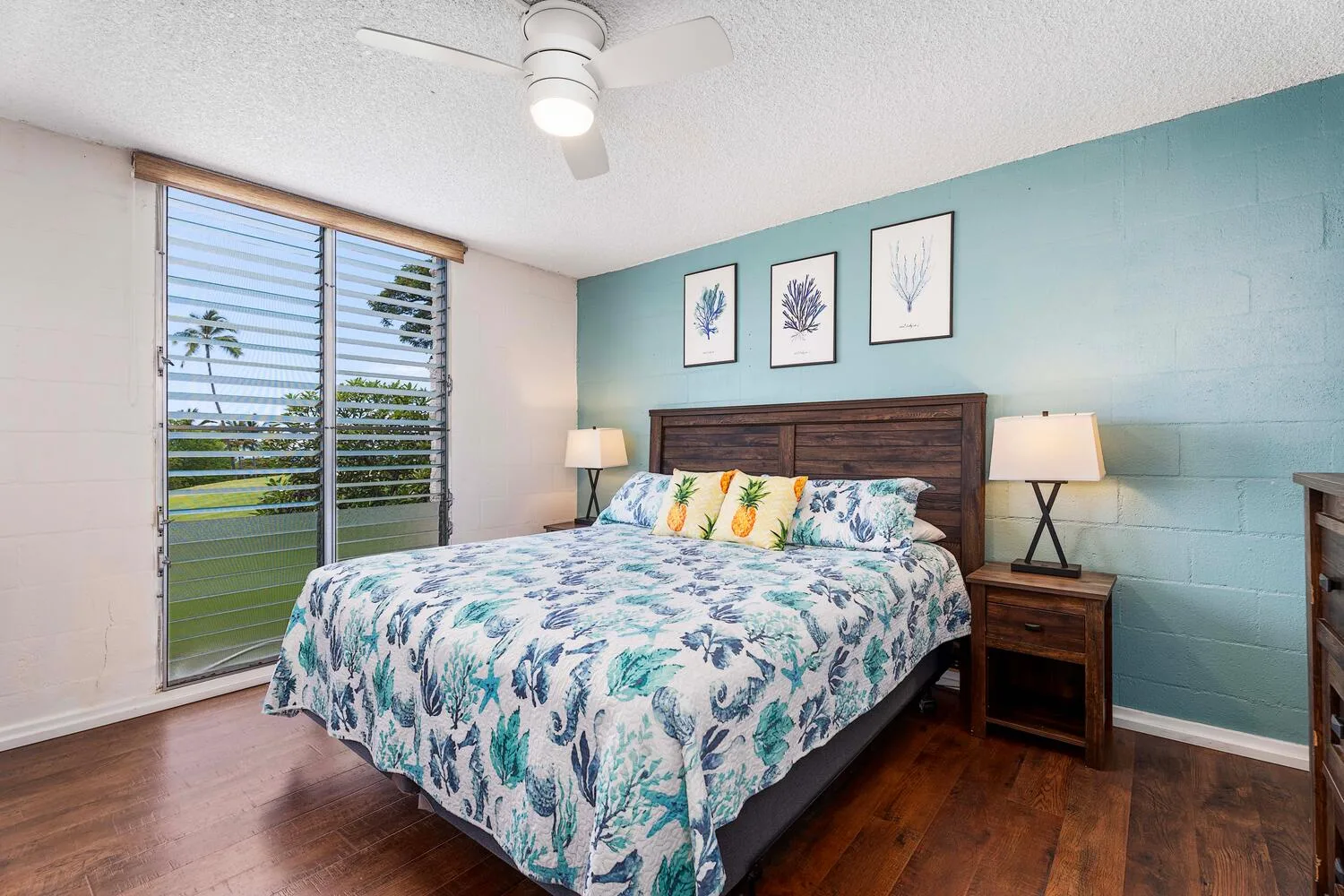 Un dormitorio con una colcha floral, mesitas de noche y una ventana grande.