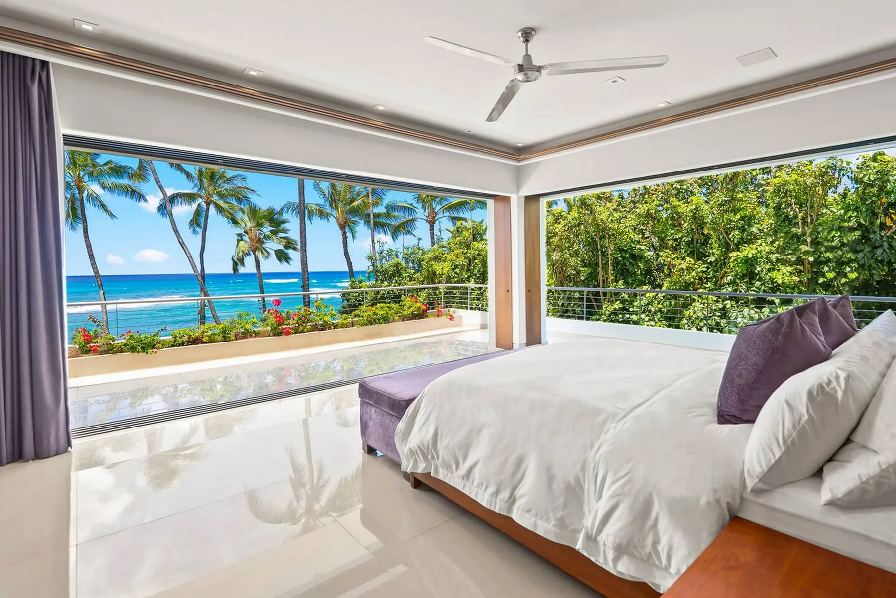 Un dormitorio luminoso se abre a un balcón con vistas a vegetación tropical y al océano.