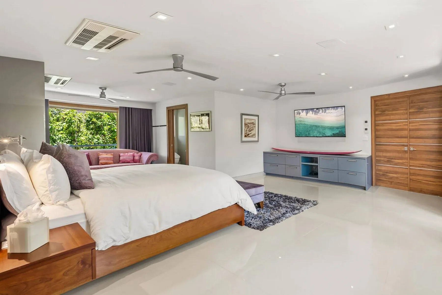 Un dormitorio luminoso con una cama grande, cuadros y un mueble bajo.