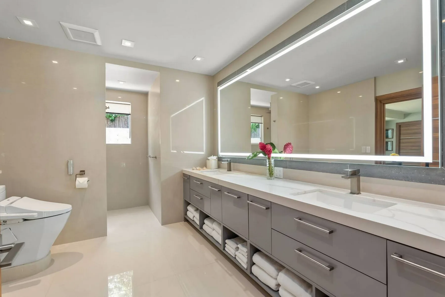 Un baño luminoso con un tocador largo, lavabo y espejo grande.
