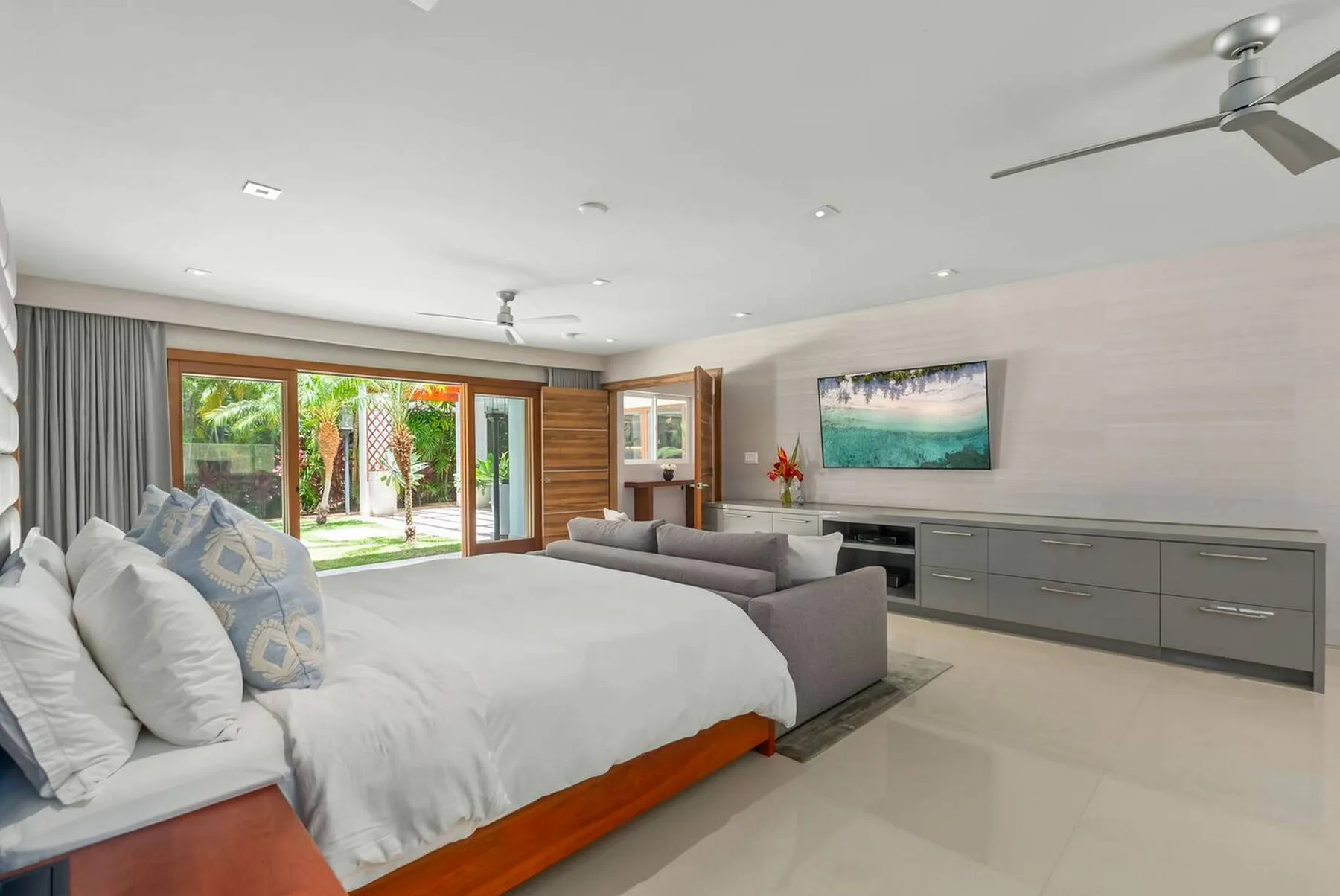 Un dormitorio luminoso con una cama grande, zona de estar y puertas de vidrio hacia un jardín.