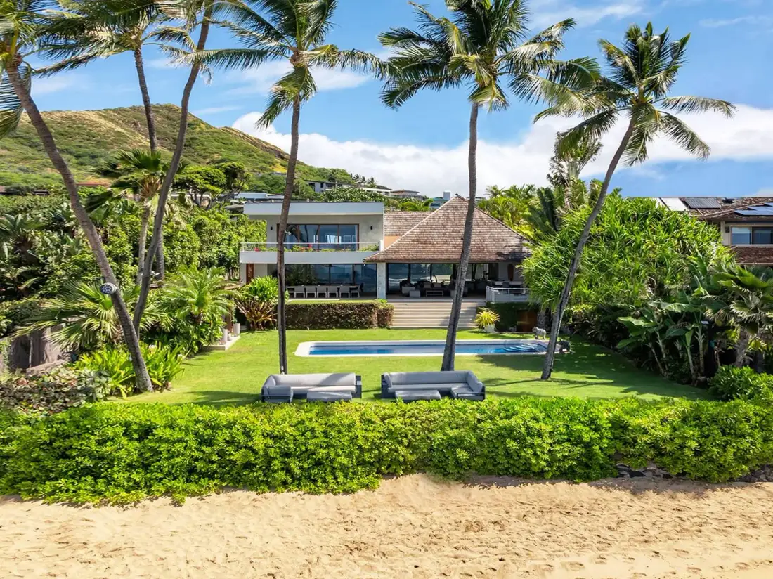 Una propiedad tropical con piscina, palmeras y arena en primer plano.