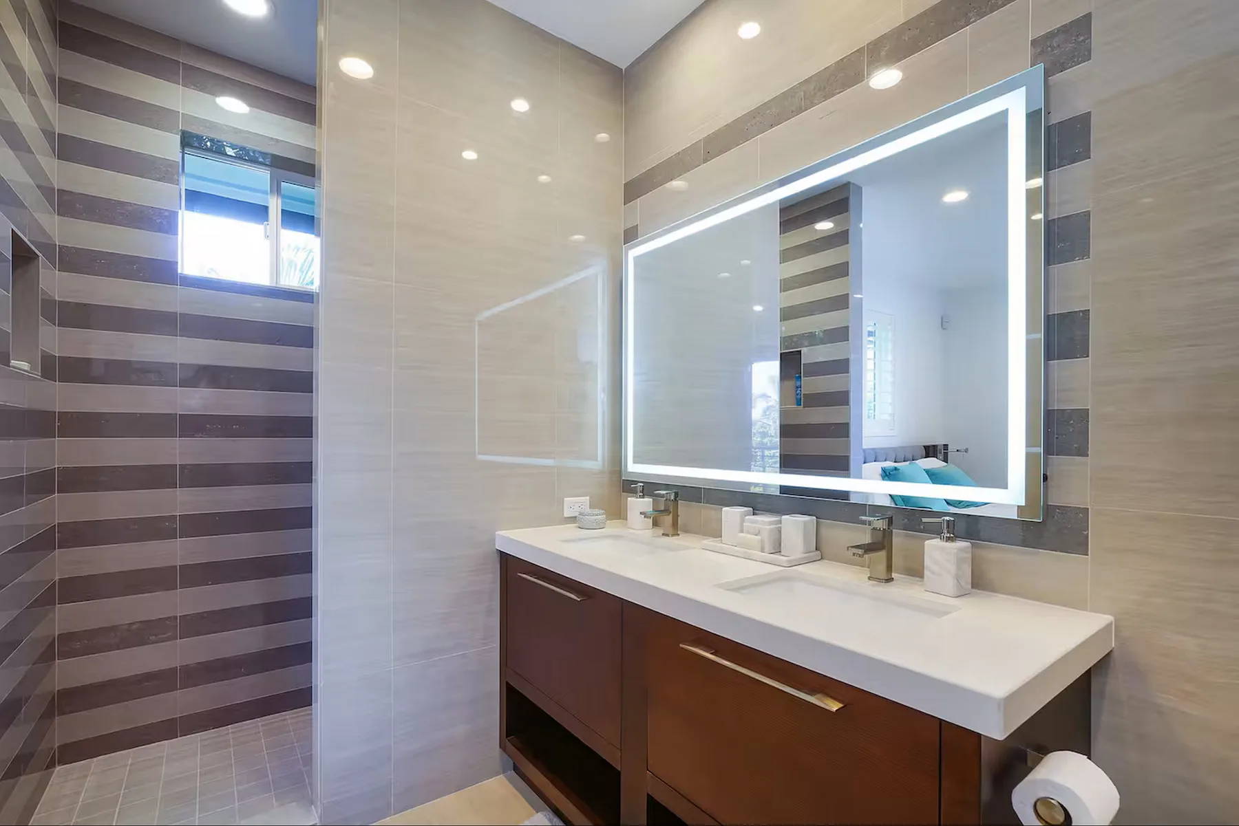Un baño revestido de azulejos tiene un tocador largo y un gran espejo iluminado.