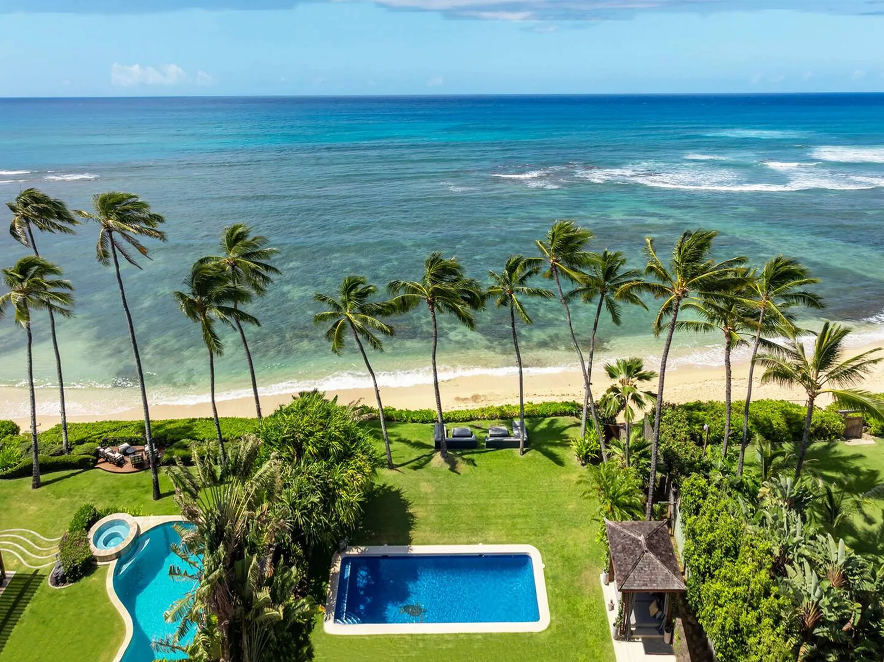 Vista aérea de una propiedad tropical frente al mar, con palmeras y piscinas.