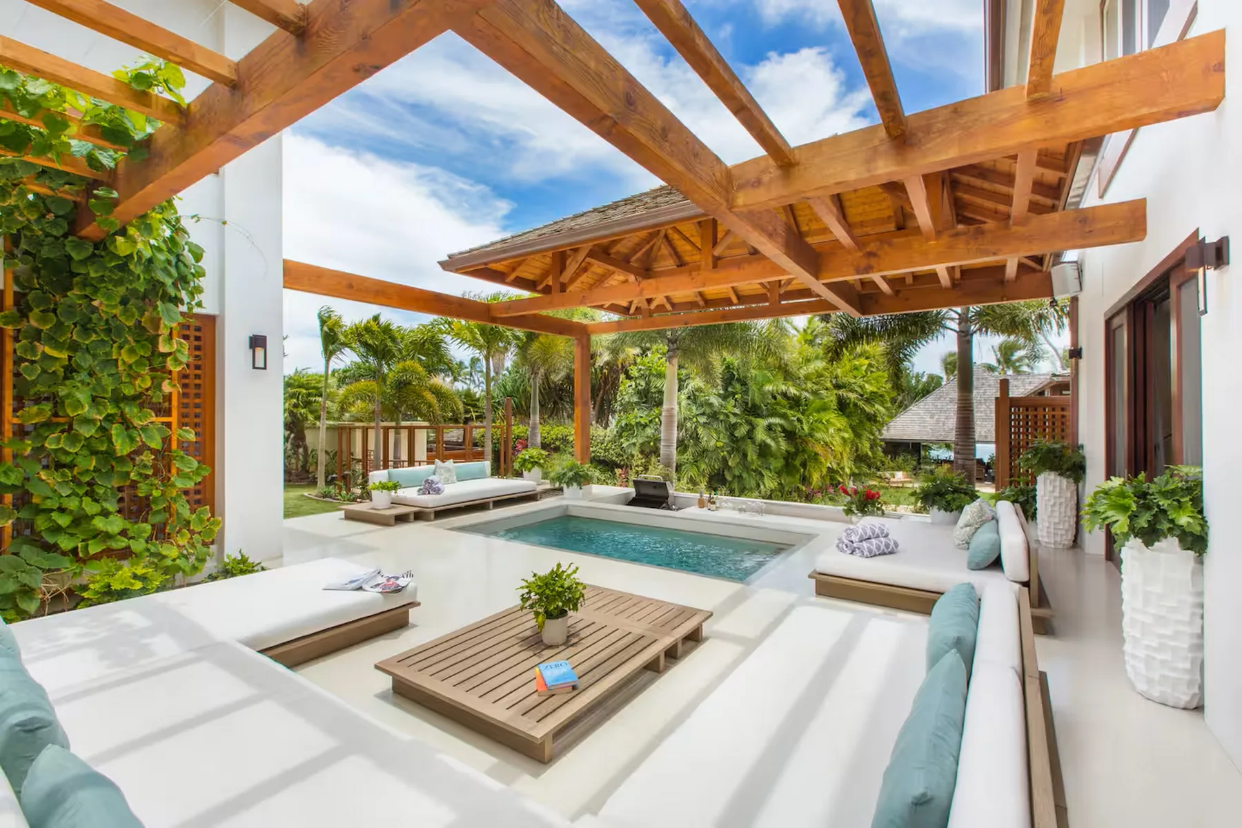 Un patio al aire libre con piscina, asientos acolchados y una pérgola de madera.