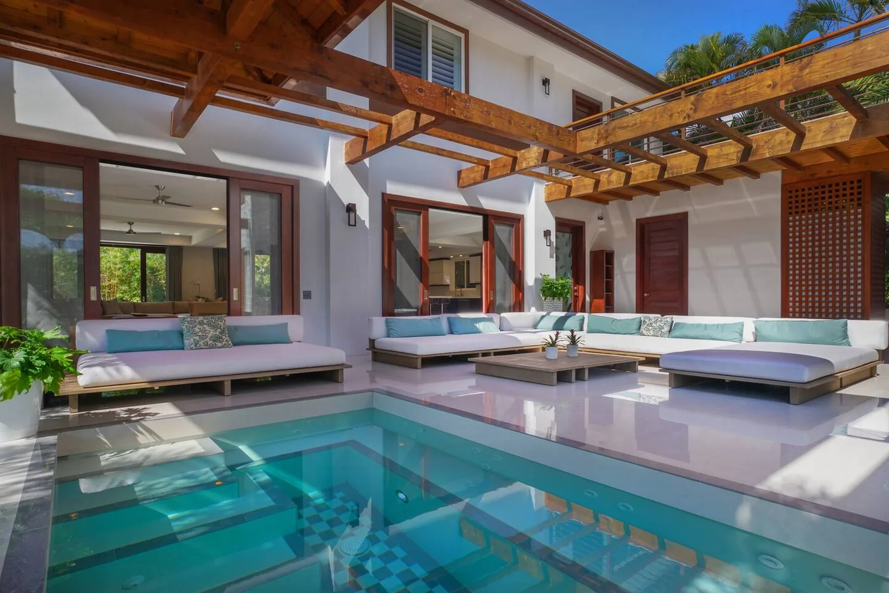 Una piscina en el patio está junto a una zona de estar al aire libre bajo vigas de madera.