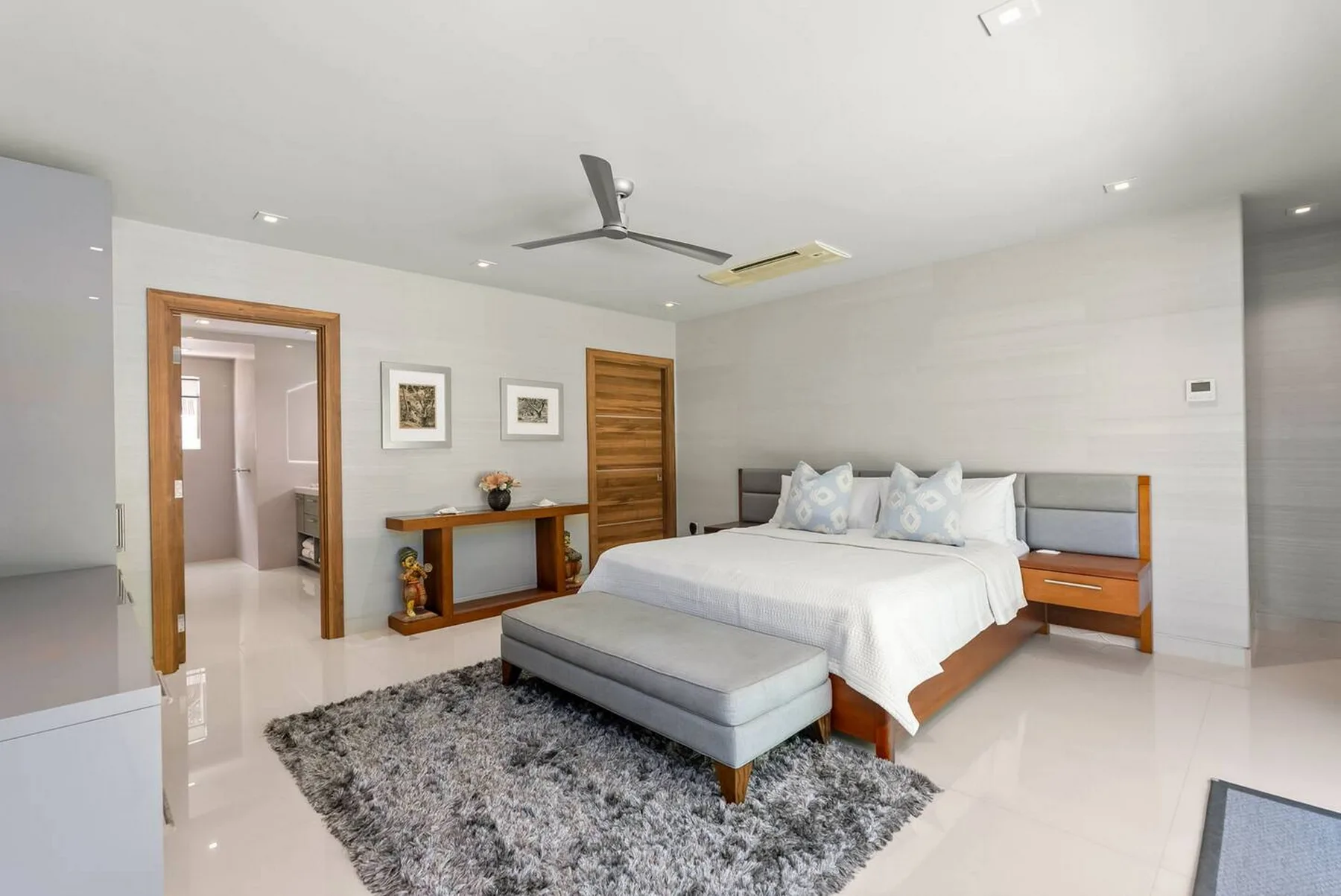 Un dormitorio luminoso con una cama grande, un banco tapizado y una alfombra gris.