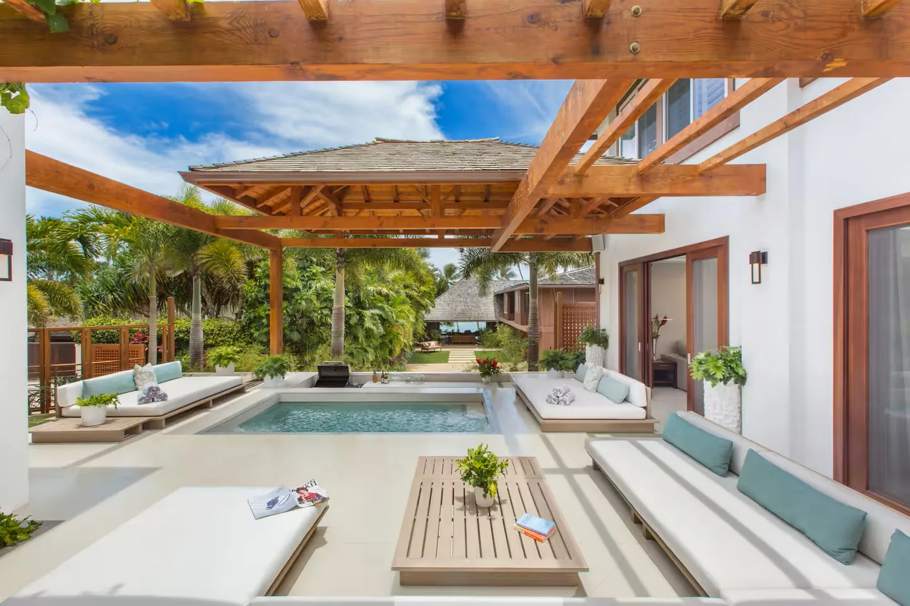 Un patio exterior con piscina, asientos integrados y una pérgola de madera.