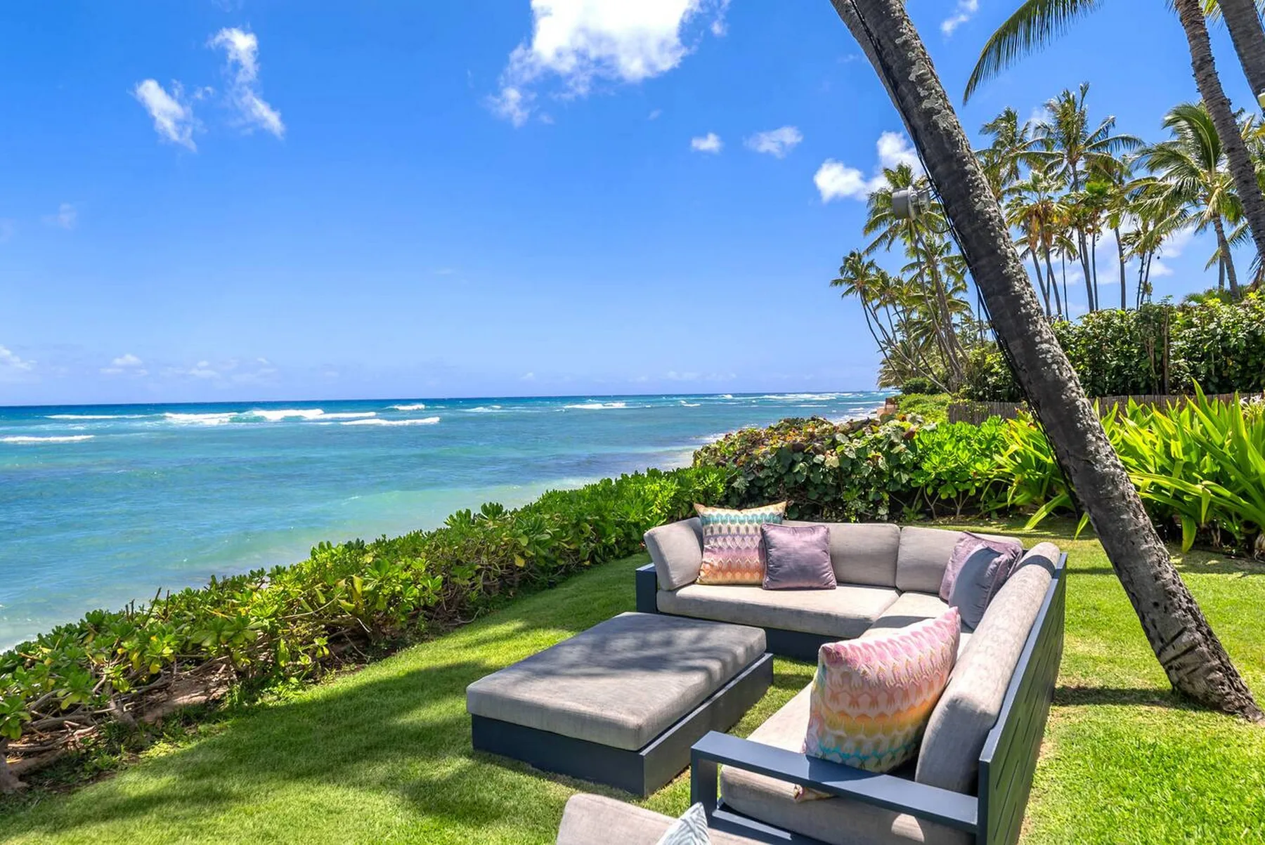 Outdoor lounge seating on a grassy lawn overlooks the ocean.