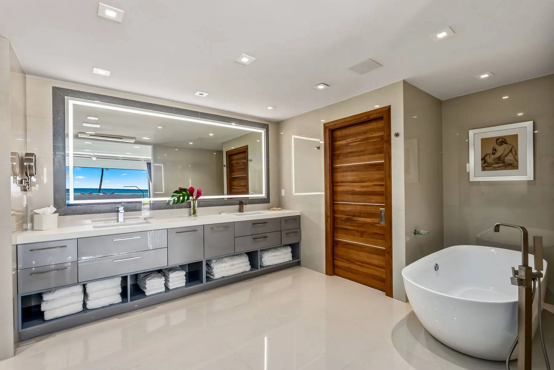 Un baño amplio tiene un tocador largo, un espejo grande y una bañera exenta.