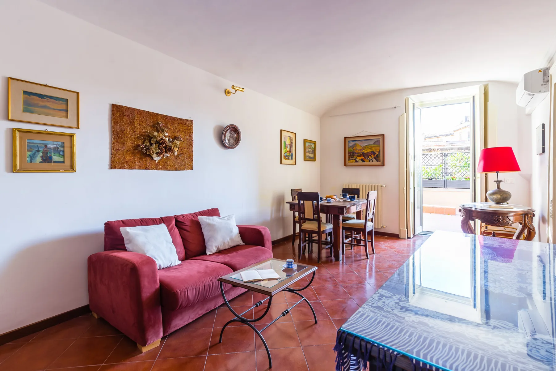 A bright living and dining room with a red sofa and a table by the open balcony door.