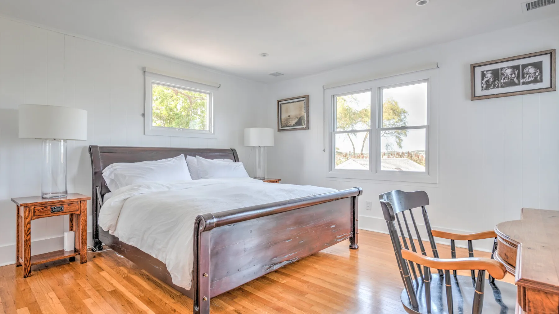 Un dormitorio luminoso con una cama de madera, ropa de cama blanca y piso de madera.