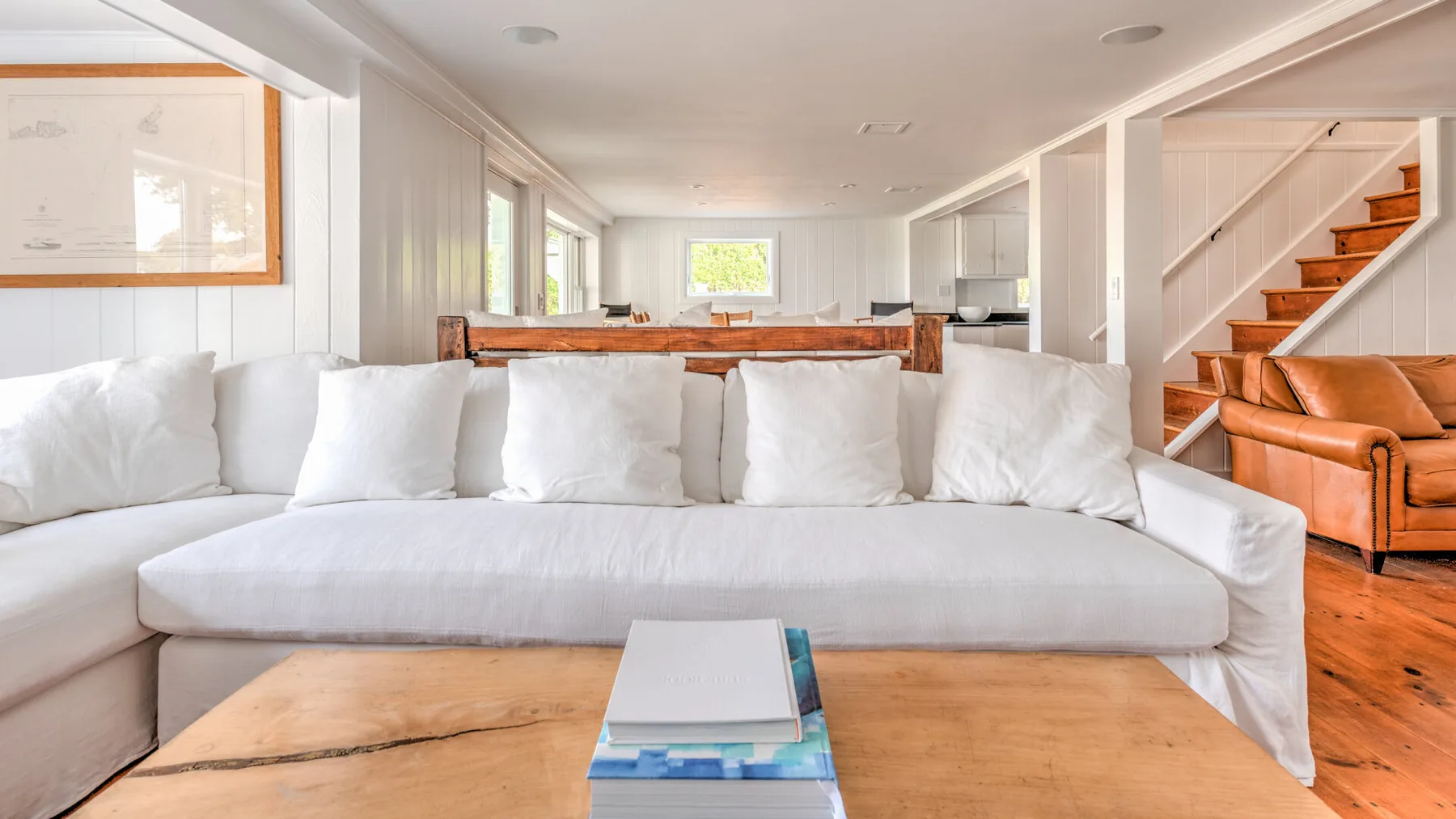 Una sala luminosa tiene una amplia zona de asientos blancos y una mesa de centro de madera.