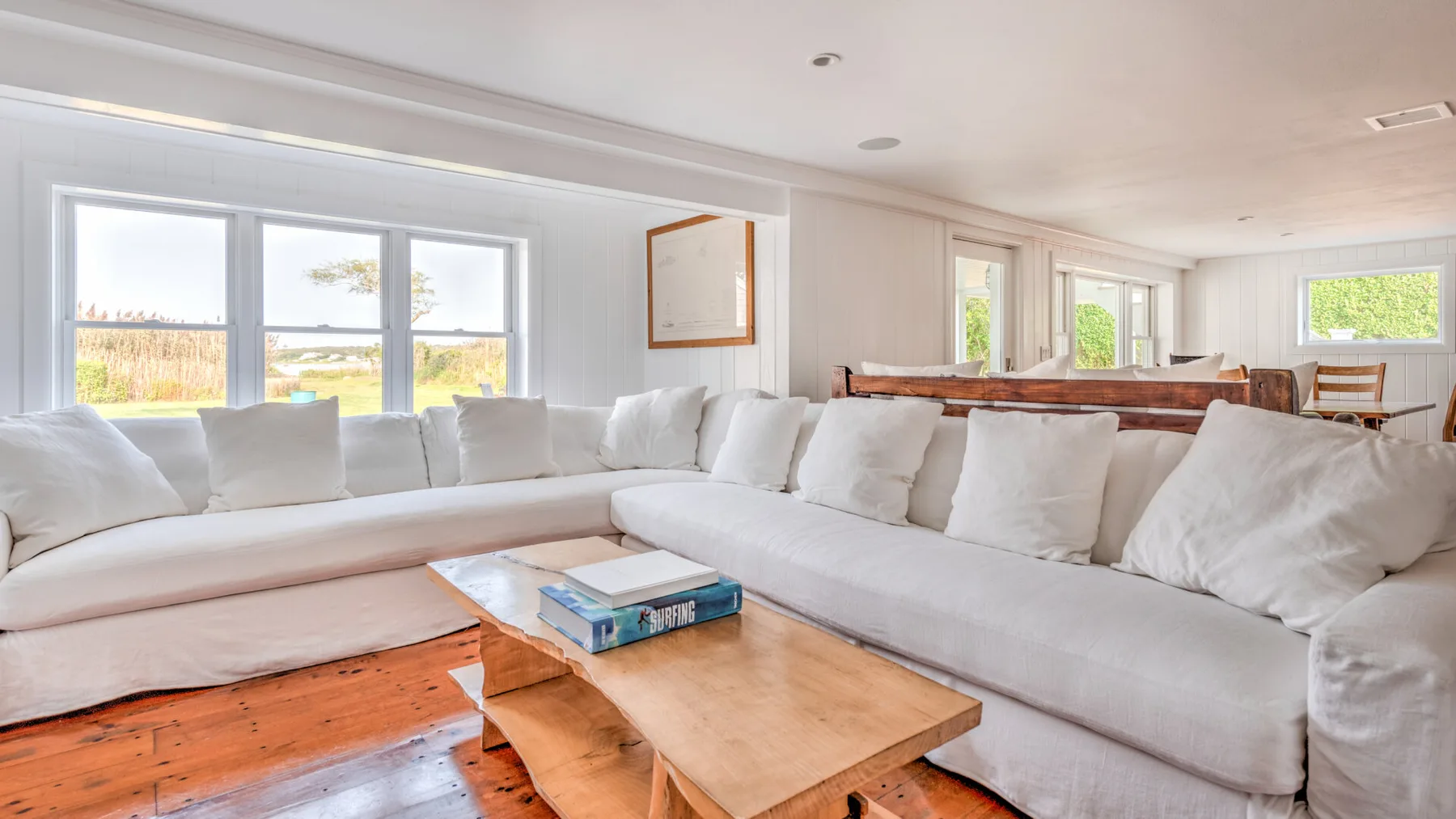 A bright living room with white seating and a wooden coffee table.