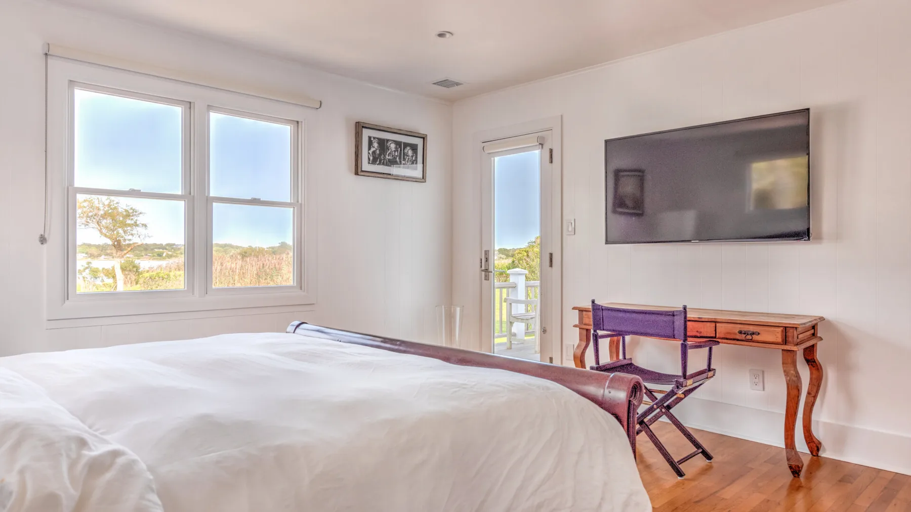 Un dormitorio luminoso con una cama, ventanas grandes y un televisor en la pared.