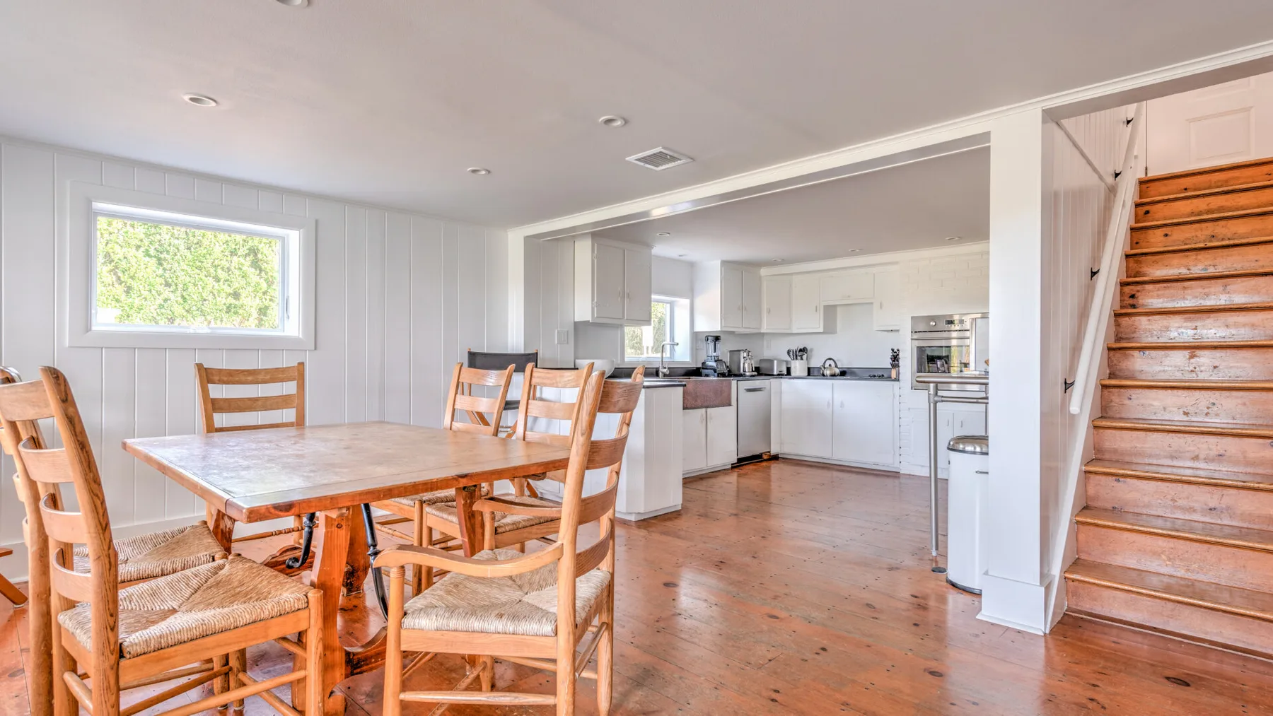Comedor abierto con cocina, una mesa de madera y una escalera.