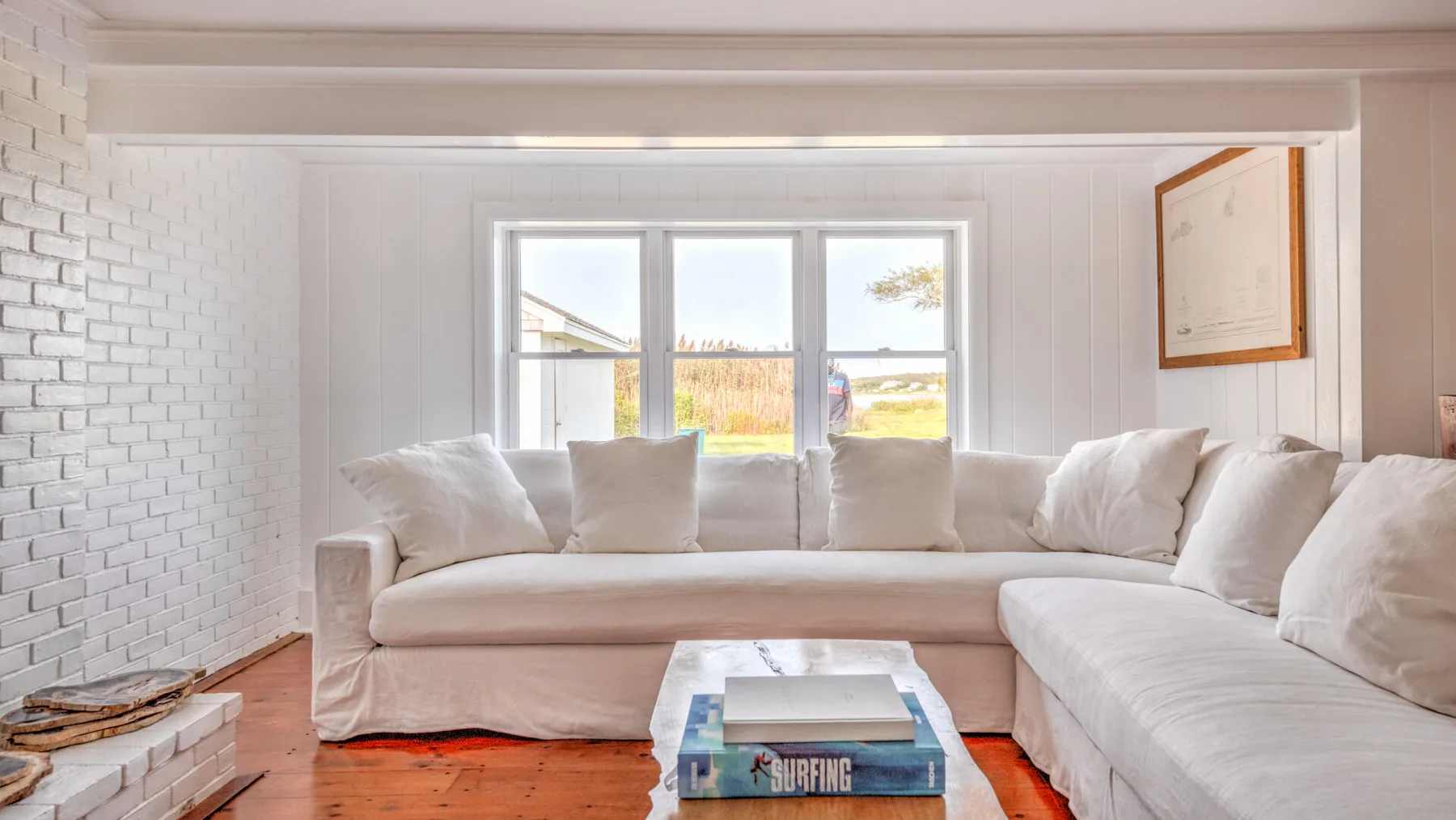 Una sala luminosa con un sofá seccional blanco junto a grandes ventanas.