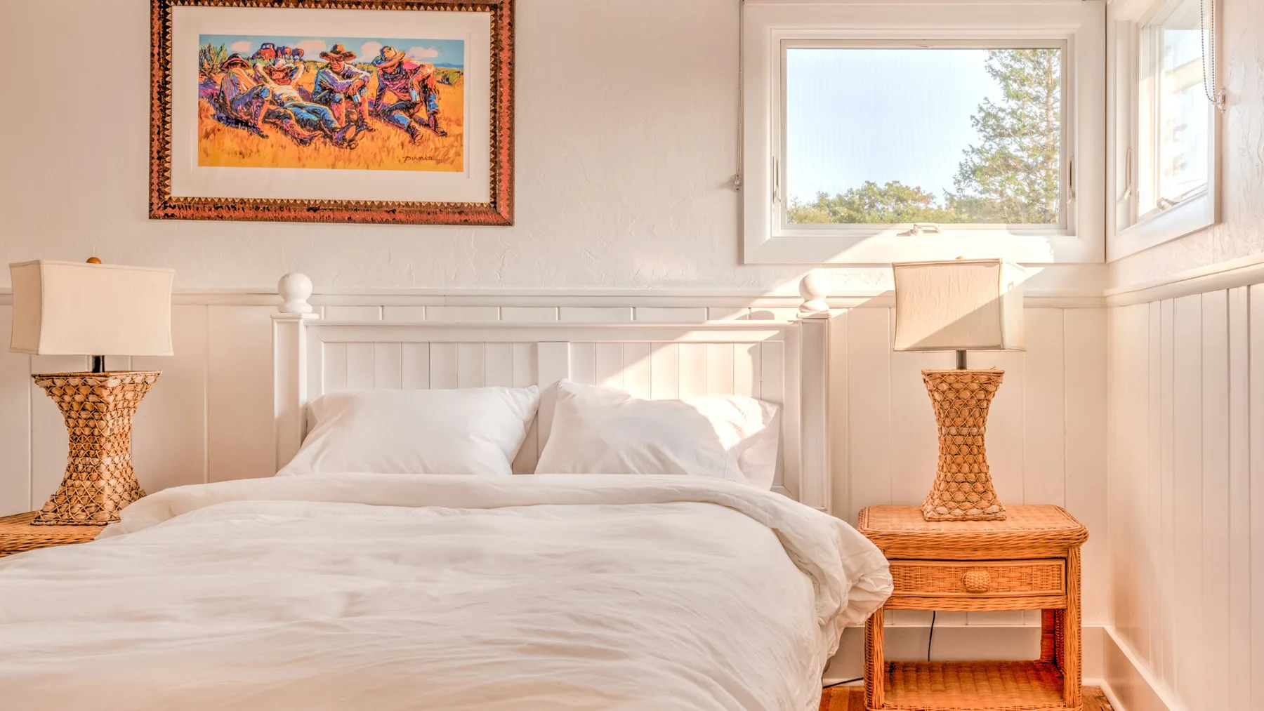 Un dormitorio con una cama blanca, mesitas de noche y ventanas.