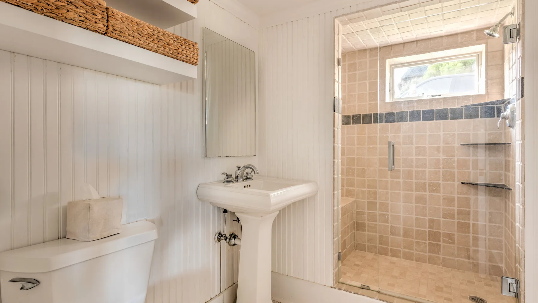 Un baño con un lavabo de pedestal junto a una ducha con azulejos.