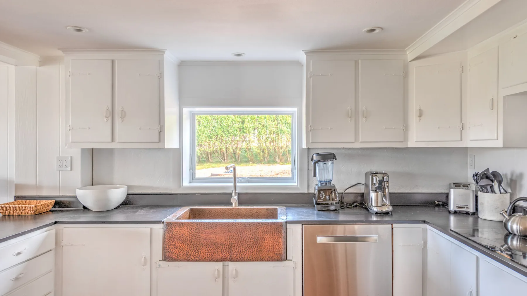 Una cocina luminosa con gabinetes blancos, una ventana central y un fregadero amplio.