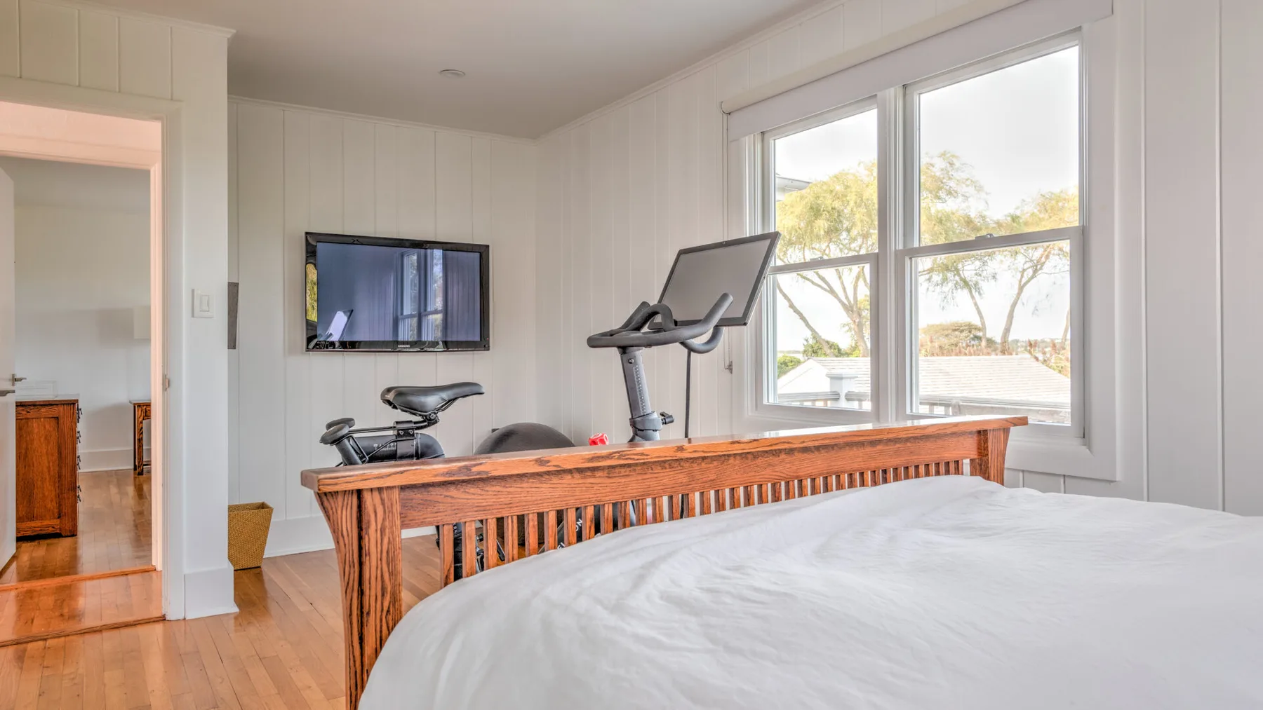 Un dormitorio luminoso con una cinta de correr y una cama junto a grandes ventanas.