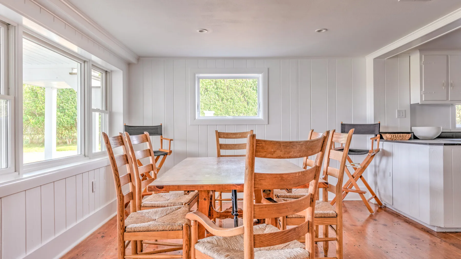 Un comedor luminoso con una mesa de madera y sillas junto a grandes ventanas.