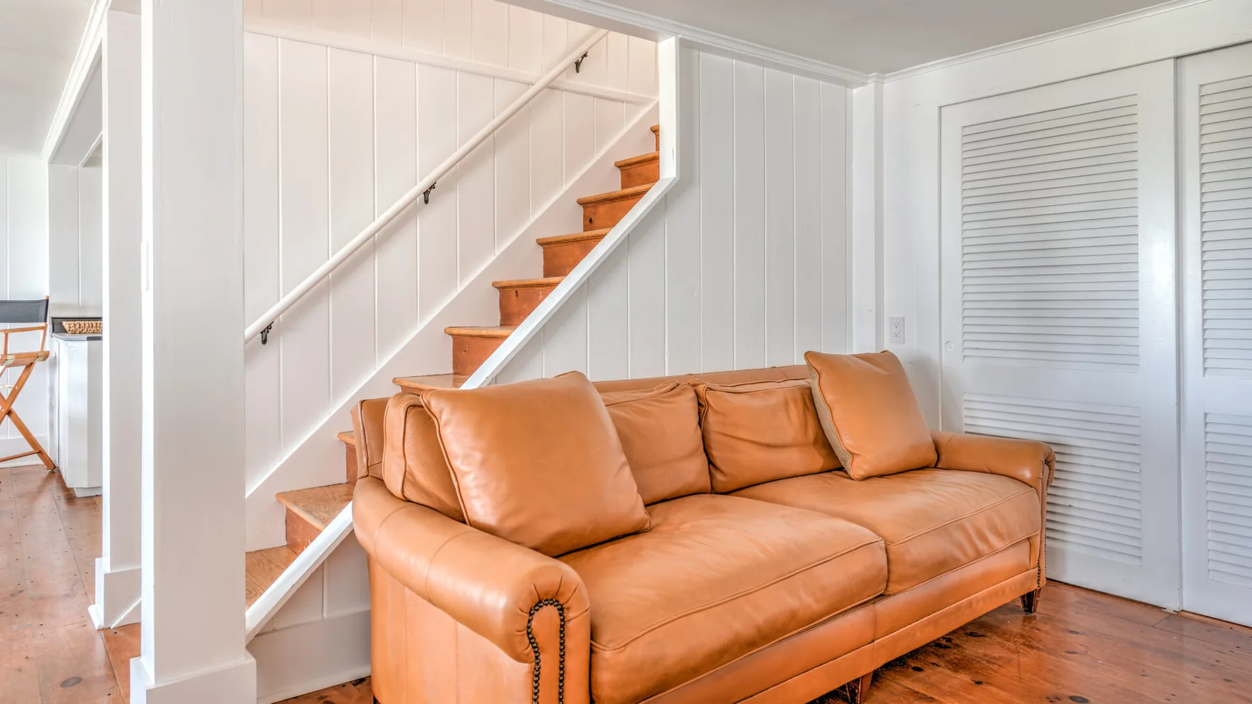 Una sala de estar con asientos color canela bajo una escalera.