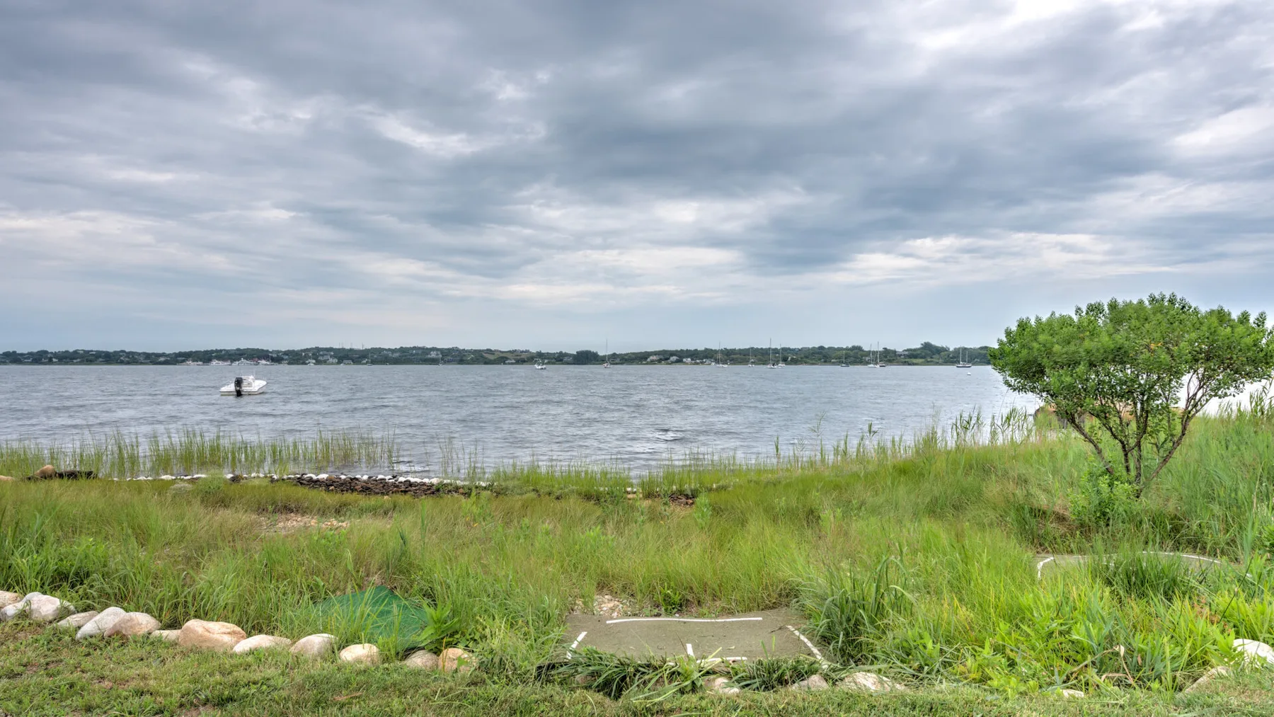 A grassy shoreline borders a calm lake beneath an overcast sky.