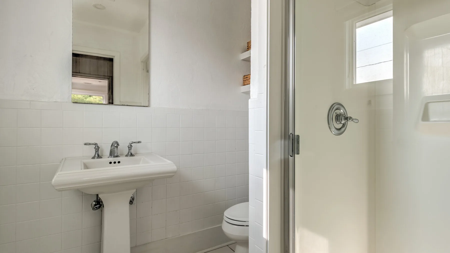 Un baño luminoso con lavabo de pedestal, espejo y ducha de vidrio.