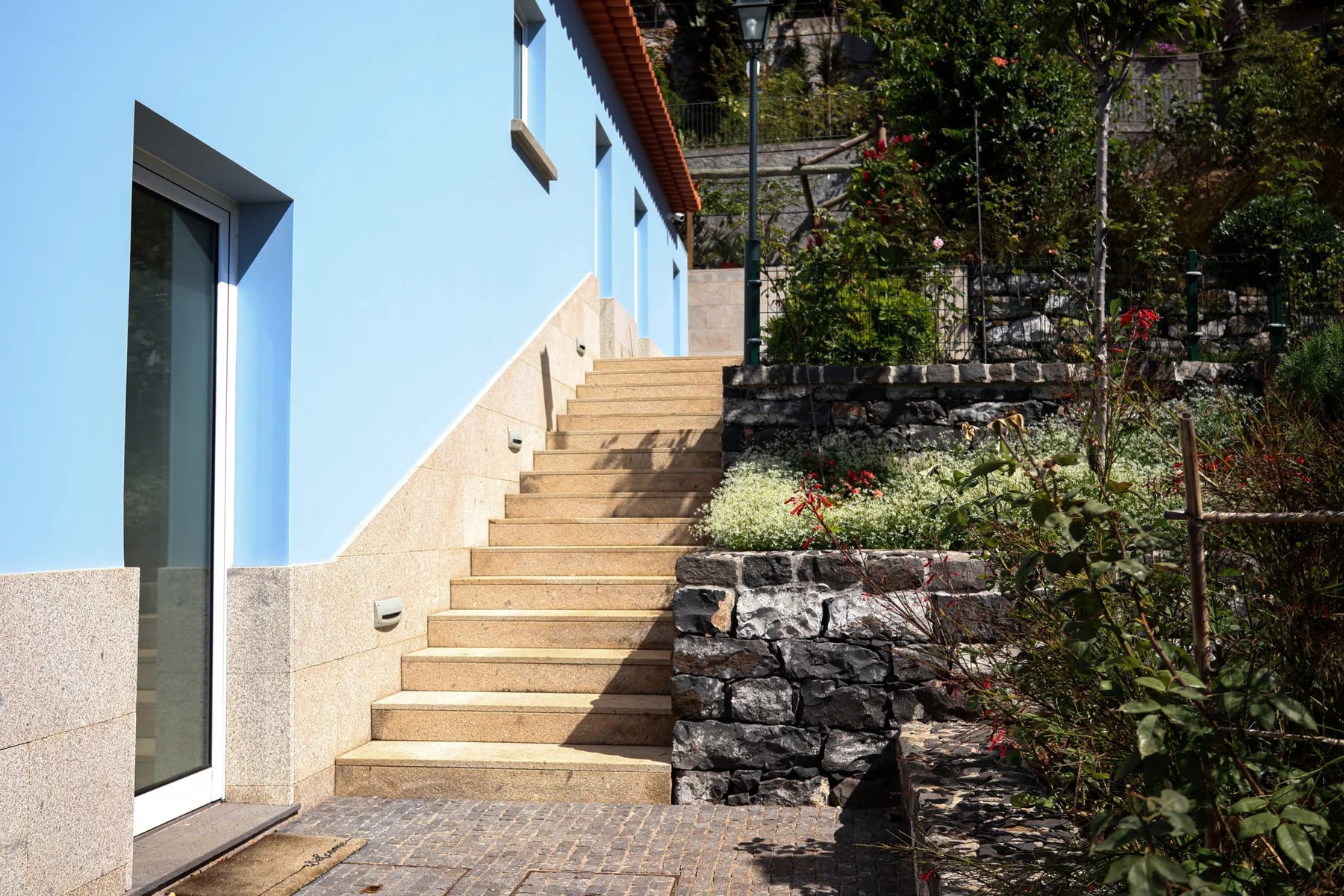 Exterior steps beside a blue house wall and a stone garden retaining wall.