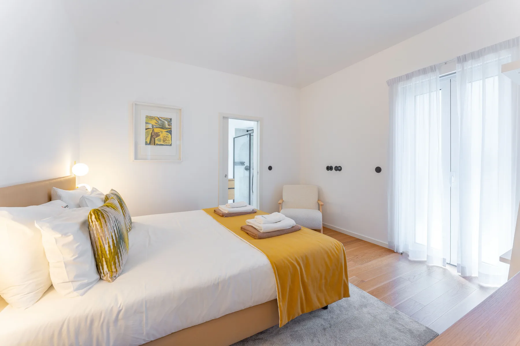 A bright bedroom with white bedding and a mustard-colored bed runner.