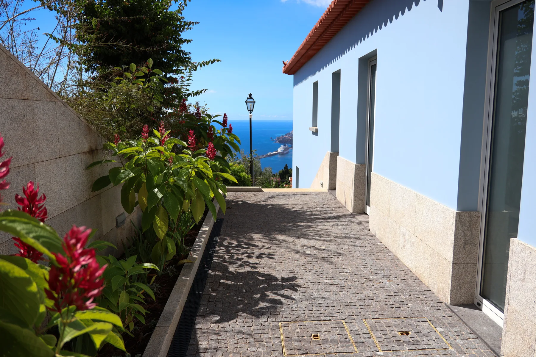 A paved walkway beside a white building overlooks the blue sea.