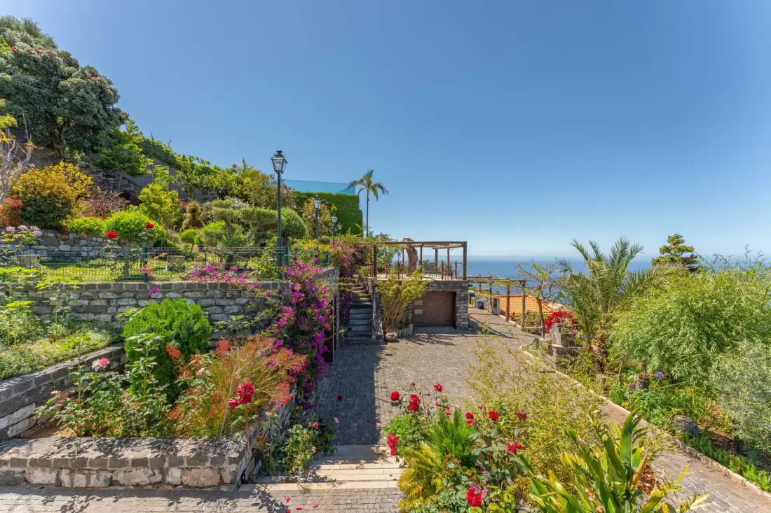 A landscaped garden path leads toward a pergola with the sea beyond.