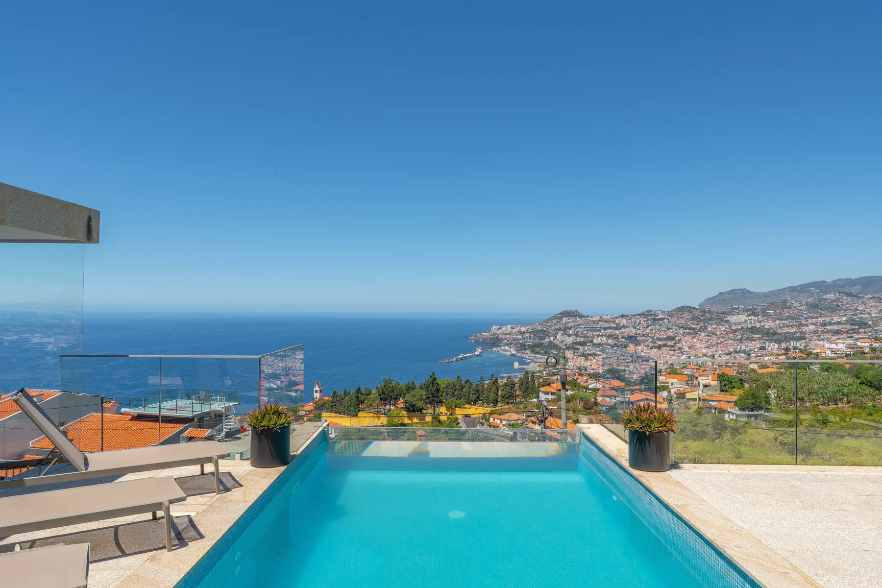 An outdoor pool overlooks the ocean and a coastal city.