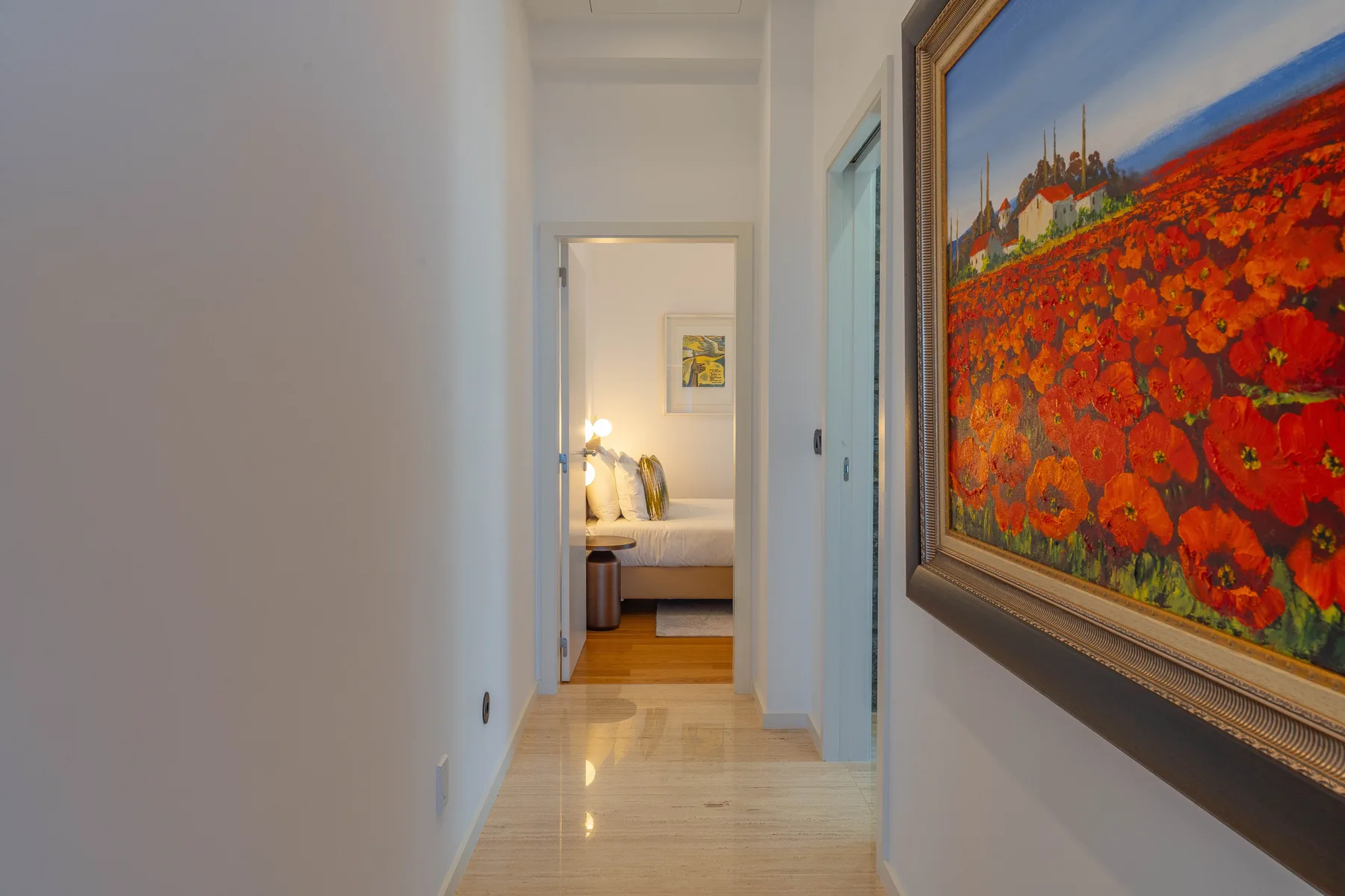 A bright hallway leads to a bedroom, with a large colorful painting on the wall.