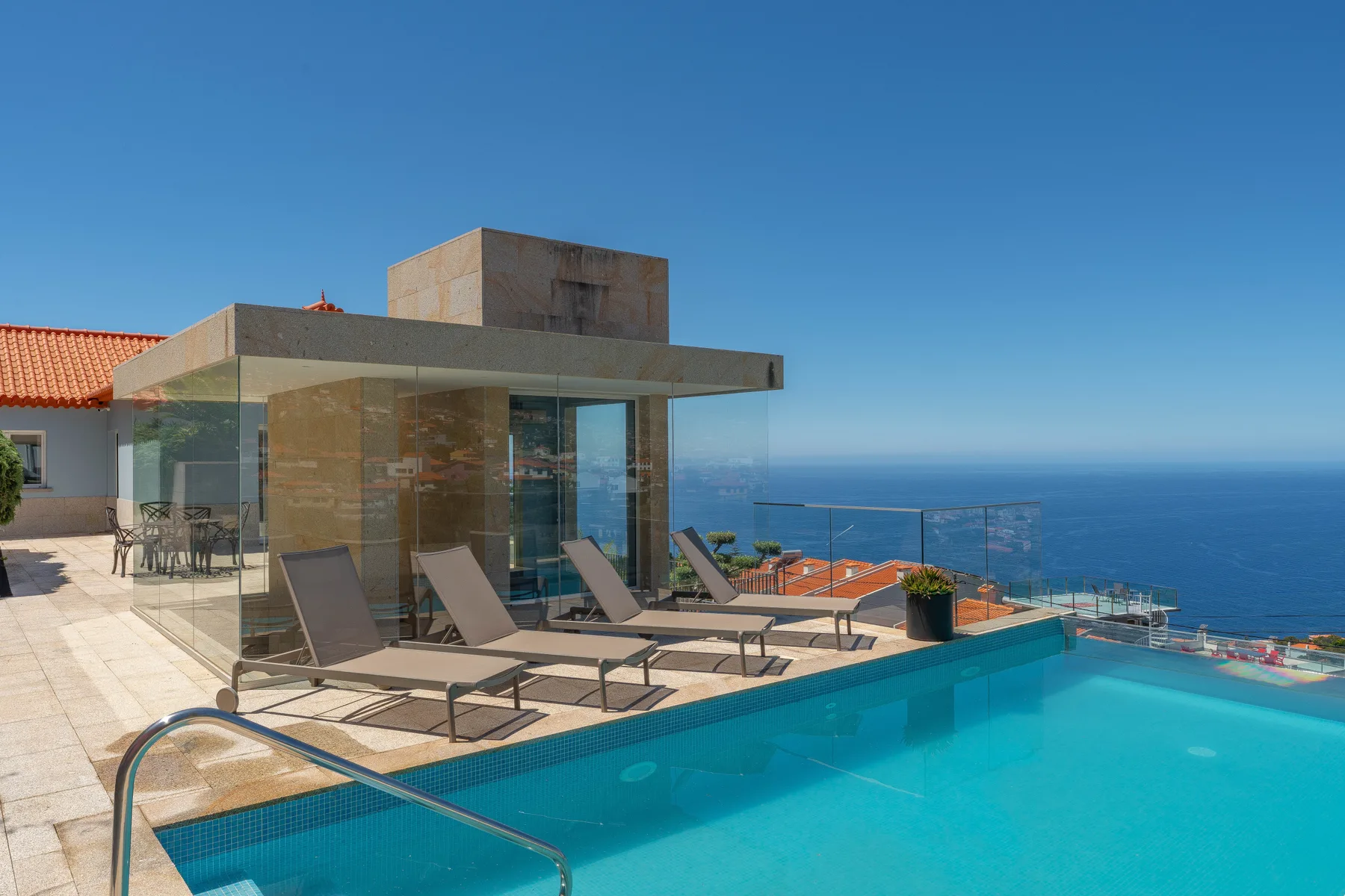 A modern glass-walled building beside a swimming pool overlooking the sea.