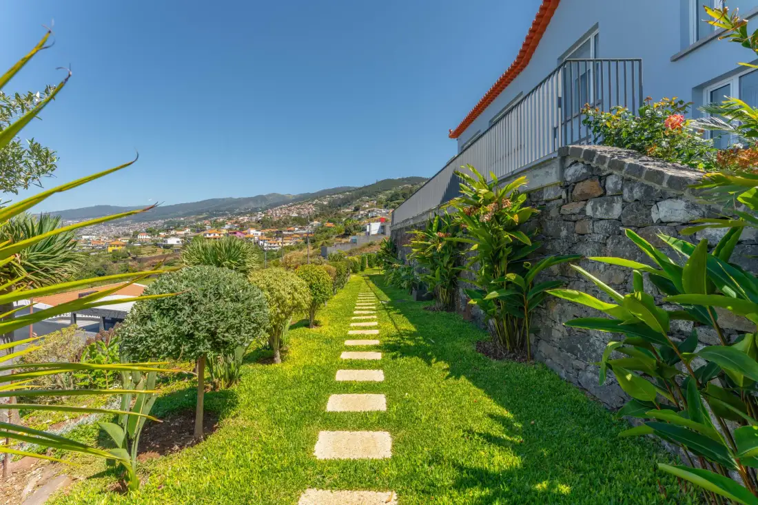 A garden path with stepping stones runs beside a house, with hills in the distance.