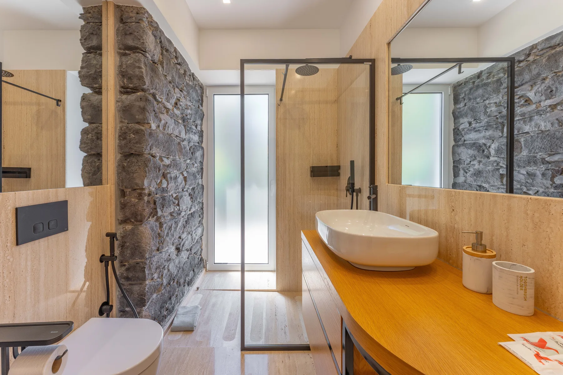A modern bathroom with a wood vanity, vessel sink, and glass shower.