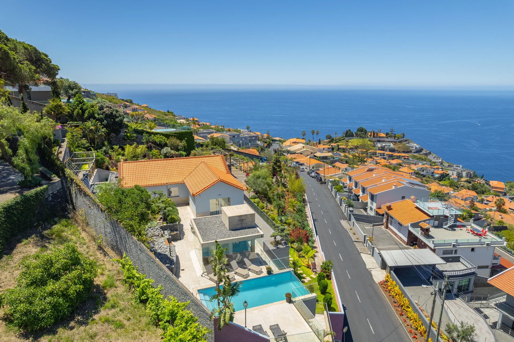 A hillside neighborhood overlooks the ocean, with a swimming pool beside a house.