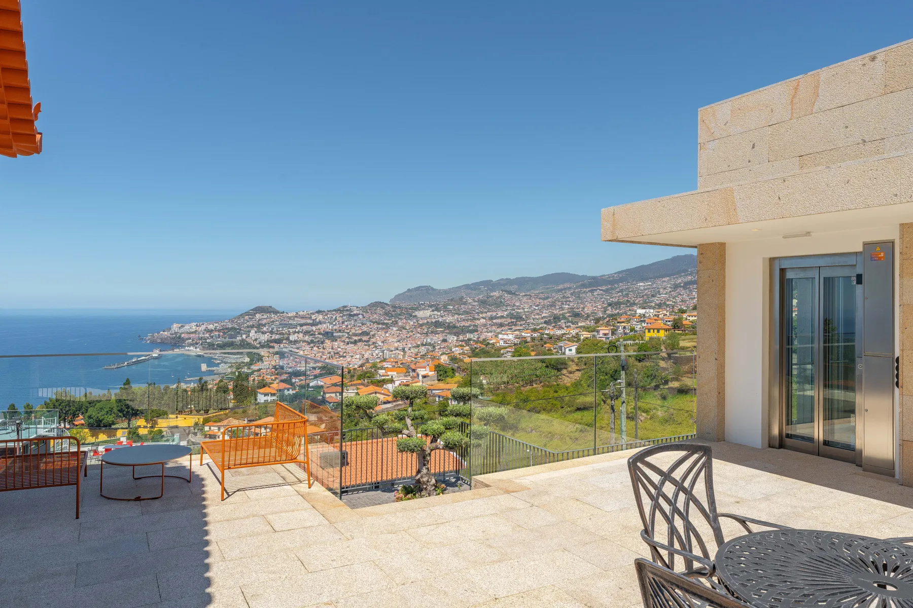 A tiled outdoor terrace overlooks the coastline and a hillside city.