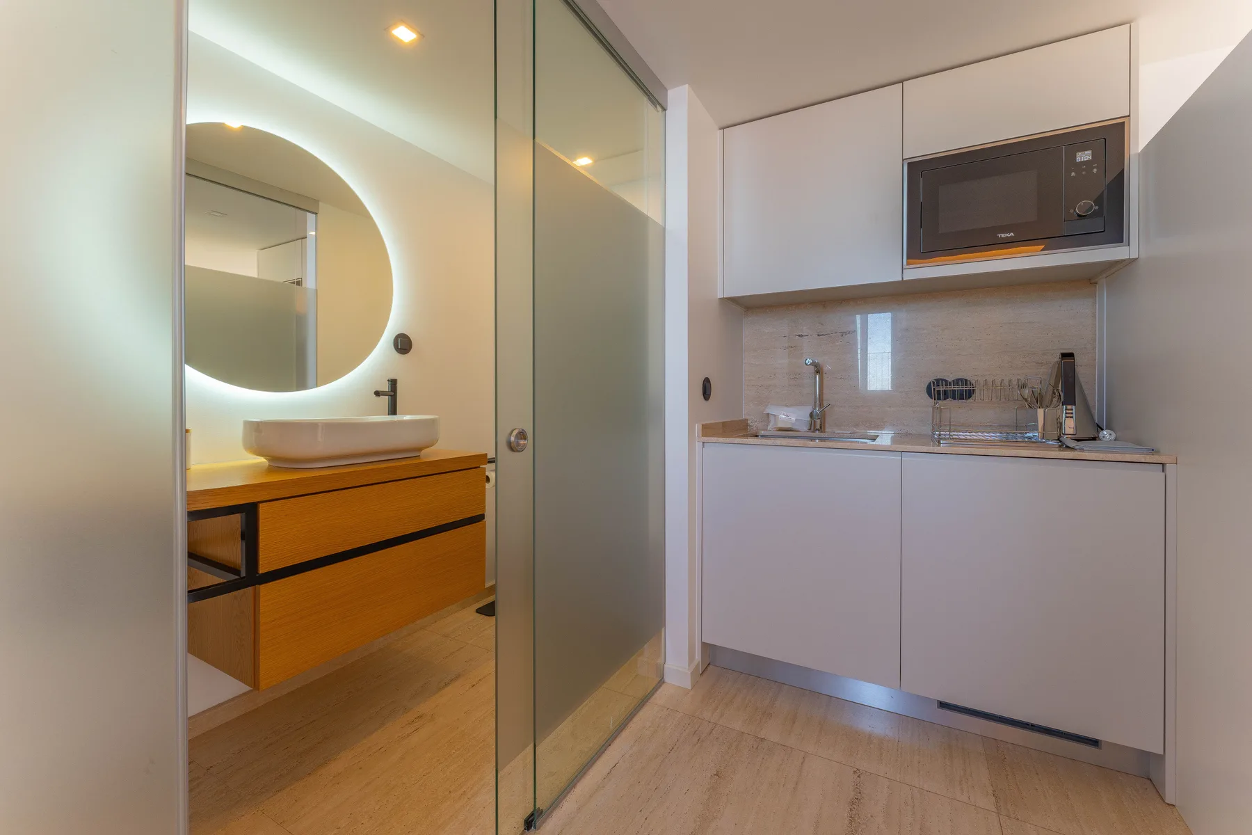 A compact kitchenette with a sink and built-in microwave sits beside a vanity.