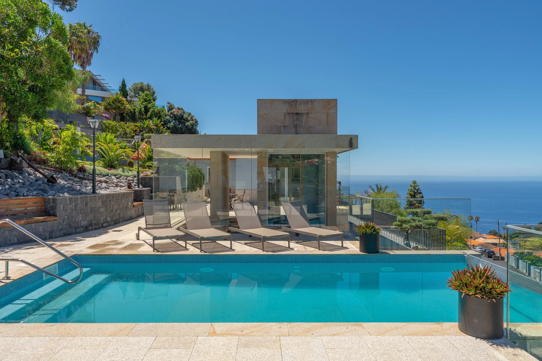 A swimming pool and modern glass-fronted pavilion overlook the ocean.