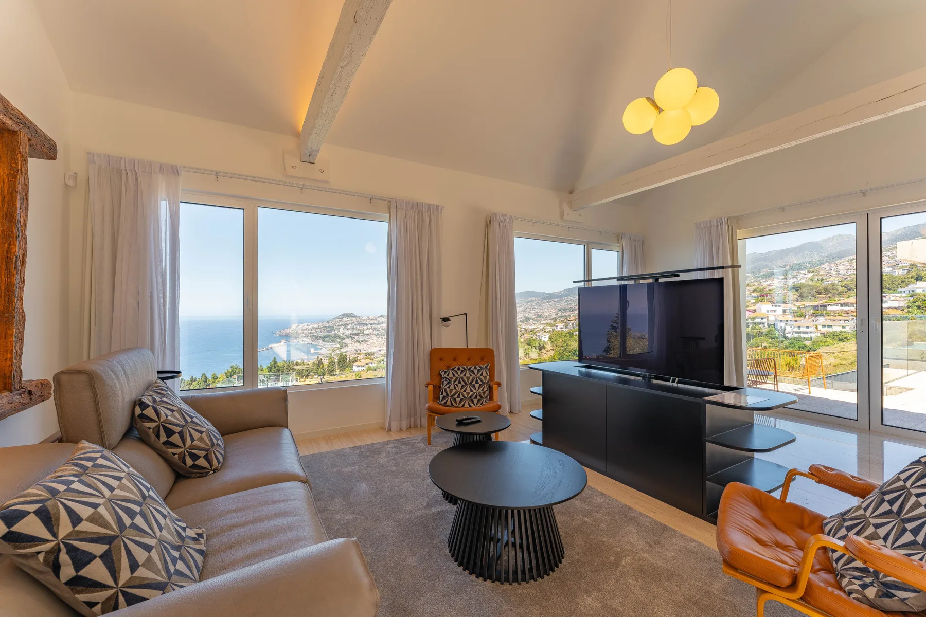 Living room with seating, a television, and broad windows overlooking the coastline.