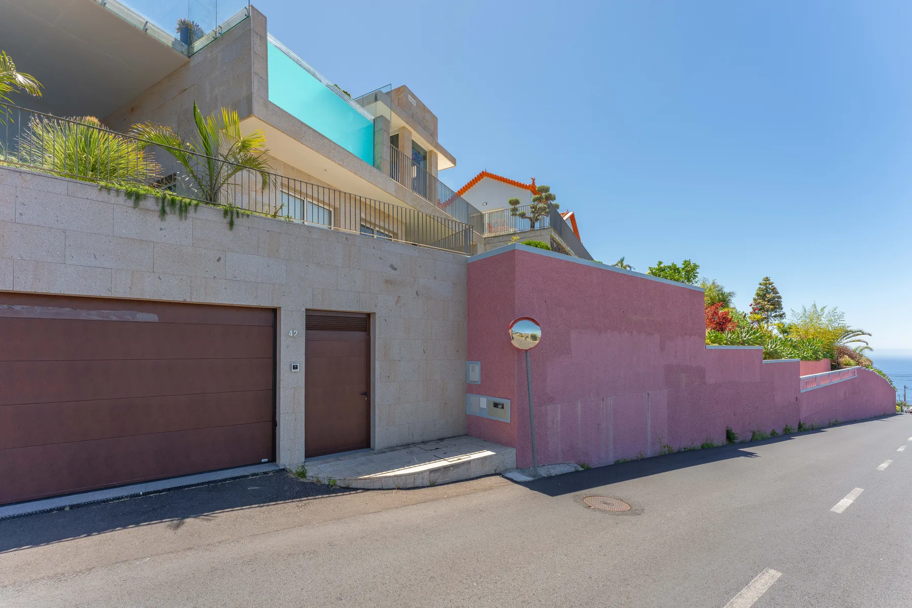 A modern house exterior with a garage and pedestrian entrance along a street.