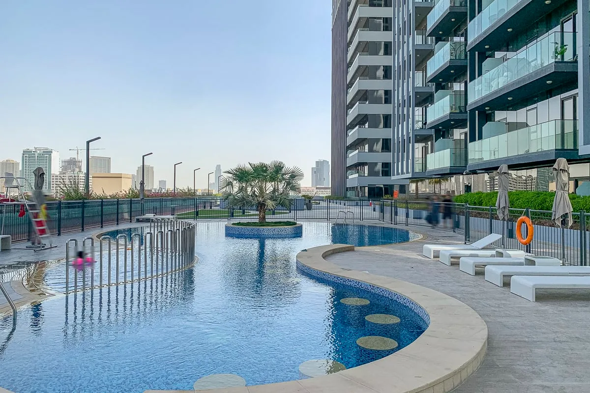 An outdoor pool beside a modern high-rise, with lounge chairs along the deck.