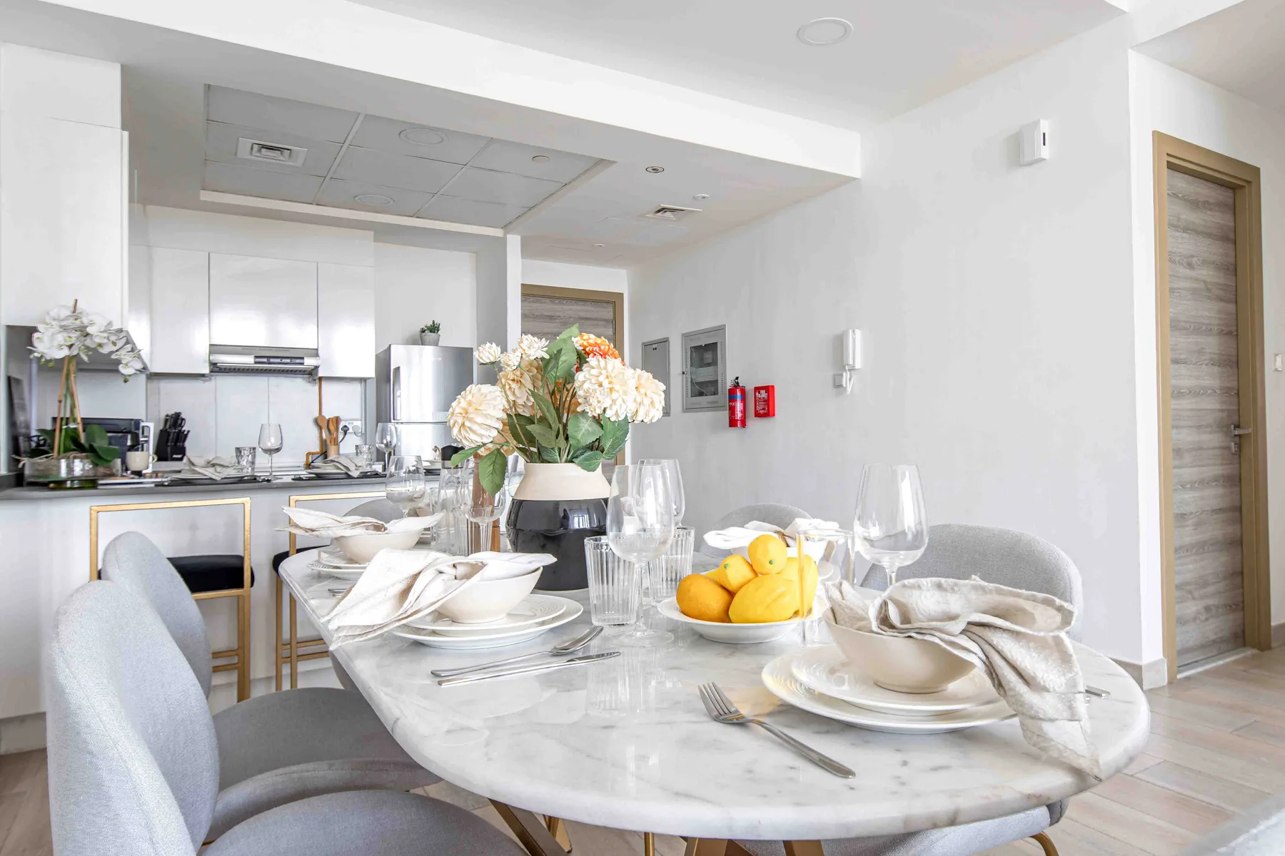 A dining table set with dishes and flowers sits beside an open kitchen.