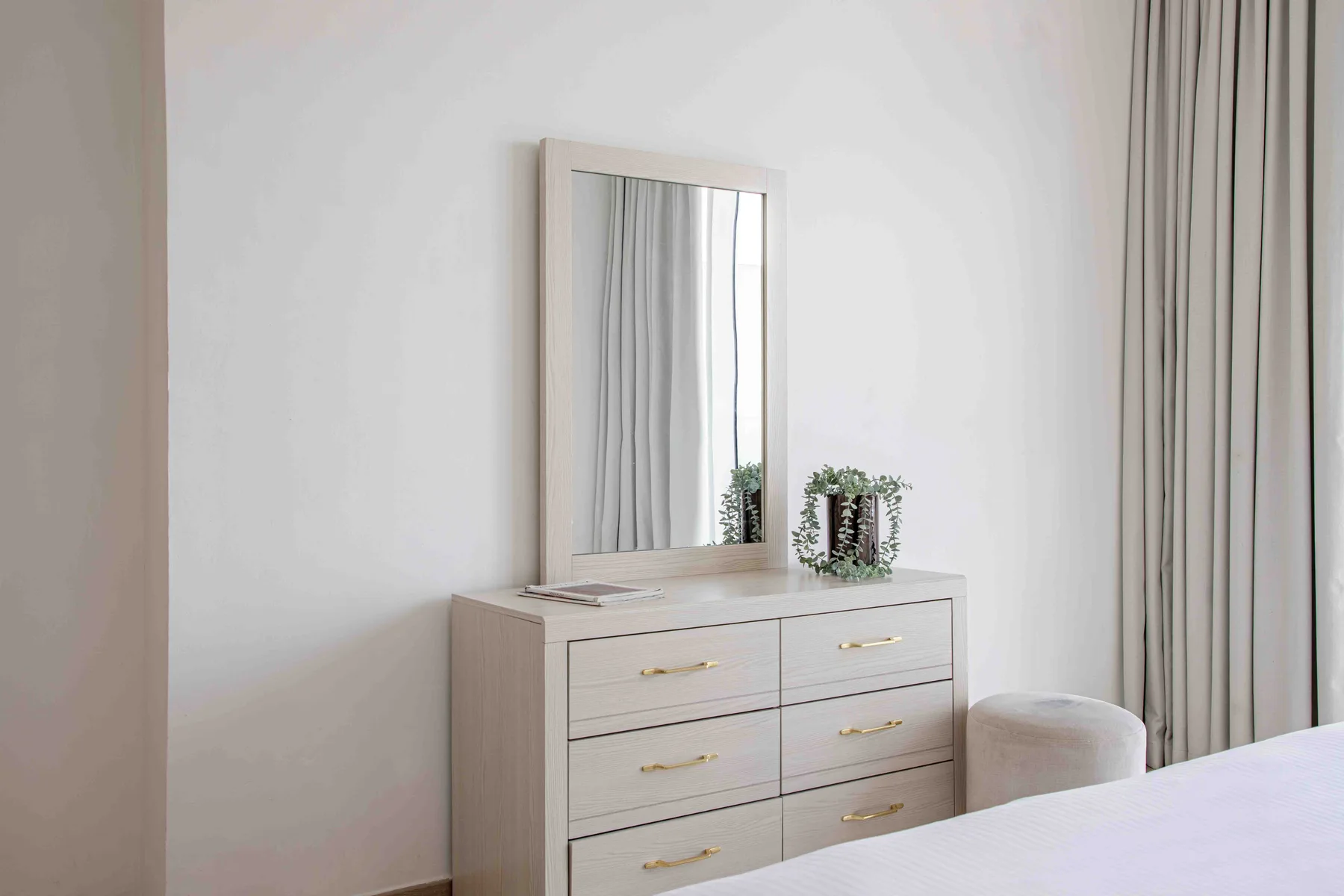 A bedroom dresser with a mirror and a small potted plant sits beside the curtains.